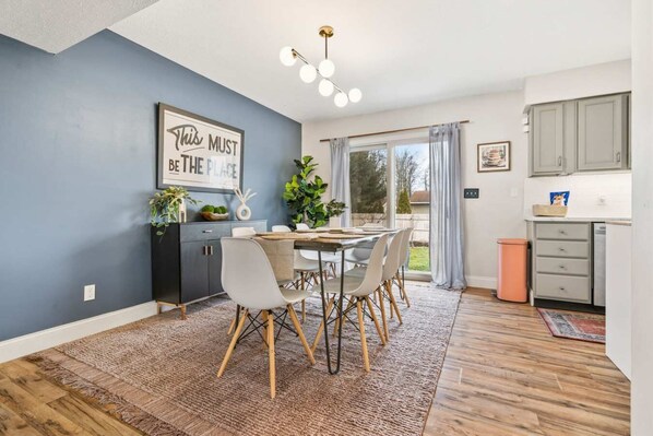 A modern kitchen with grey cabinets, a dining area with a round table and chairs, and a large window with curtains.