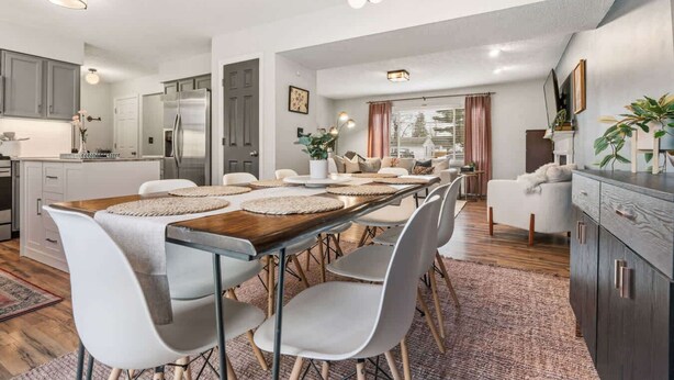A modern kitchen with white cabinets, a wooden dining table with placemats, and a seating area with white chairs. - 4 BR - Hot Tub-Game Room-Near MGM-Sleeps 8 (Northfield)