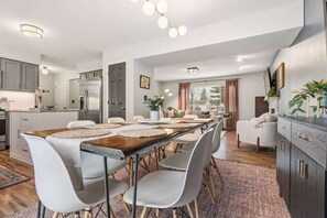 A modern kitchen with white cabinets, a wooden dining table with placemats, and a seating area with white chairs.