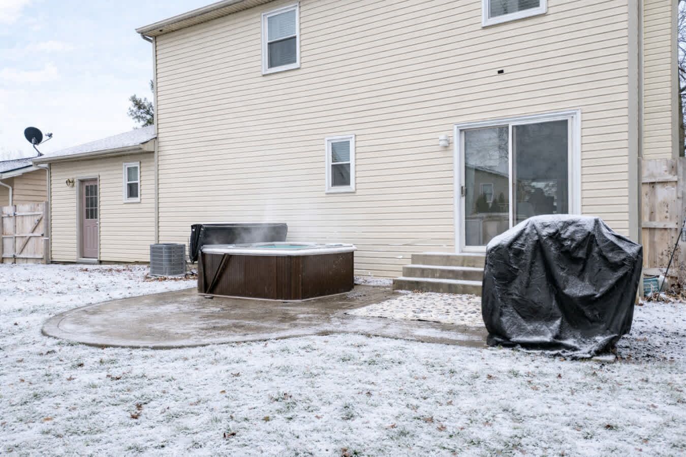 Ein Haus mit einem überdachten Whirlpool, einem überdachten Grill und einem schneebedeckten Garten.