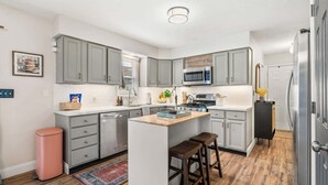 A modern kitchen with grey cabinets, a central island, bar stools, and a microwave. - 4 BR - Hot Tub-Game Room-Near MGM-Sleeps 8 (Northfield)