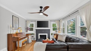 Een woonkamer met een open haard, een bank, een piano en een plafondventilator.