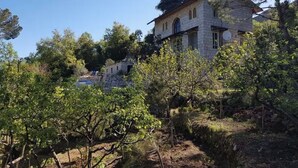 Une maison en pierre avec un toit en pente, entourée d’arbres et d’un jardin.