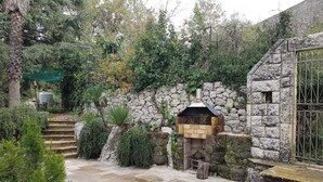 Un espace extérieur aménagé en pierre, avec un mur en pierre, une petite structure en bois et un portail en métal.