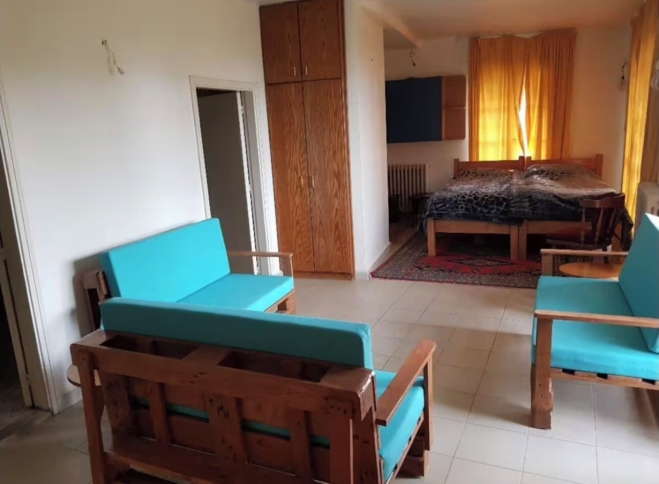A room with a bed, two wooden chairs with blue cushions, a wardrobe, and a television.