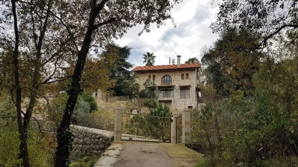 Un bâtiment en pierre avec un toit rouge, entouré d’arbres et d’un mur de pierre.