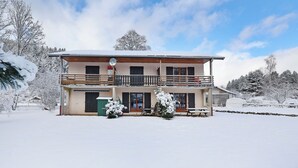 A two-story building with a balcony, a covered outdoor seating area, and snow-covered trees. - Chez Valentin (Gérardmer)