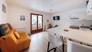 A modern kitchen with white cabinetry, a dining table, and a sofa. - Chez Valentin (Gérardmer)