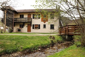 A two-story building with a balcony, a wooden staircase, and a small garden area with a stream. - Chez Valentin (Gérardmer)