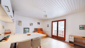 A spacious room with a white table, two chairs, a wooden desk, and a sofa with orange cushions. - Chez Valentin (Gérardmer)