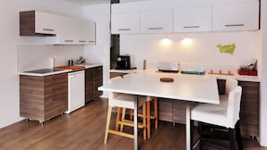 A modern kitchen with white cabinets, a white countertop, and a wooden dining table with bar stools. - Chez Valentin (Gérardmer)
