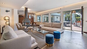 Un salon moderne avec un canapé, des poufs, une table basse en verre et une cheminée.