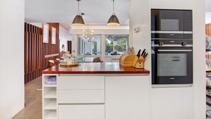 Une cuisine moderne dotée d’un four encastré, de luminaires suspendus et d’un îlot central en bois.