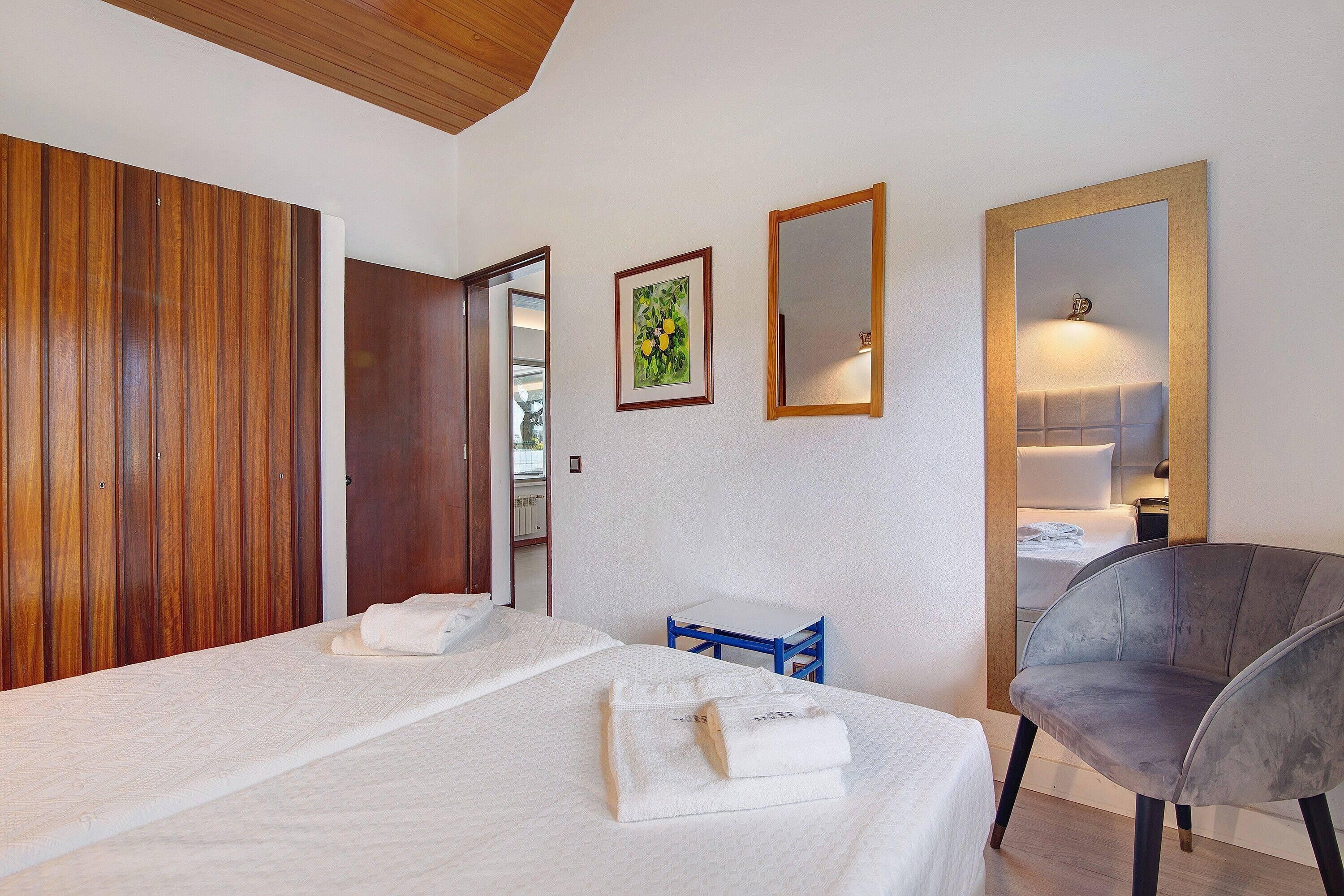 A hotel room with a bed, a chair, a small table, a mirror, and wooden paneling on one wall.