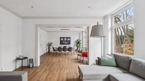 Un salon moderne avec un canapé, un coin repas comprenant une table et des chaises, et de grandes fenêtres donnant sur la verdure.