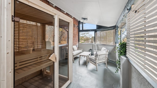 Une terrasse extérieure couverte, aménagée avec du mobilier en bois, dotée d’une porte-fenêtre coulissante et offrant une vue sur les environs.