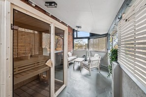 Eine überdachte Terrasse im Freien mit Holzmöbeln, einer Glasschiebetür und Blick auf die Umgebung.