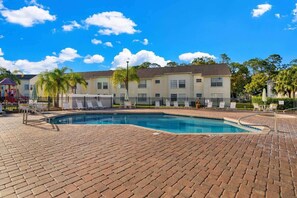 A swimming pool with a brick deck, a fenced area with lounge chairs, and a row of buildings in the background. - Resort Pool*Renovated*Near Parks! (Kissimmee)