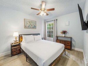 A bedroom with a bed, nightstand, lamp, ceiling fan, window, and a wall-mounted TV. - Resort Pool*Renovated*Near Parks! (Kissimmee)