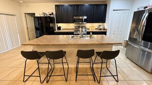 A modern kitchen with dark cabinets, stainless steel appliances, a granite countertop, and four bar stools. - Charming 3-bedroom house with AC in peaceful neighborhood, minutes from Disney! (Dundee)
