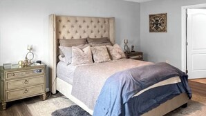 A bedroom with a tufted headboard, a bed with multiple pillows, a bedside table with a lamp, and a decorative wall piece. - Charming 3-bedroom house with AC in peaceful neighborhood, minutes from Disney! (Dundee)