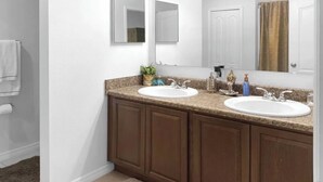 A bathroom with two sinks, a large mirror, and brown cabinets. - Charming 3-bedroom house with AC in peaceful neighborhood, minutes from Disney! (Dundee)