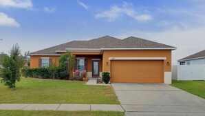 A single-story house with a garage, a front porch, and a well-maintained lawn. - Charming 3-bedroom house with AC in peaceful neighborhood, minutes from Disney! (Dundee)