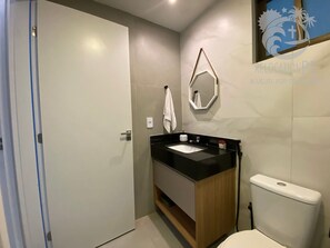 Une salle de bain moderne avec un lavabo sur un plan de toilette noir, un meuble-lavabo en bois, des toilettes blanches et un miroir avec un cadre géométrique.