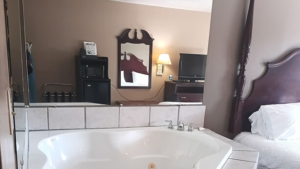 A bathroom with a large bathtub, a wooden headboard, and a mirror. - Oak Tree Inn (Durant)