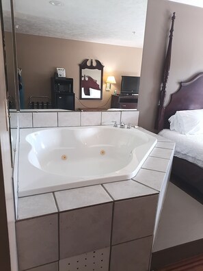 A bathroom with a large bathtub, a wooden headboard, and a mirror. - Oak Tree Inn (Durant)
