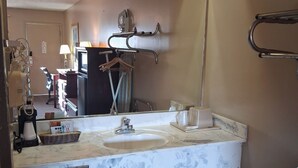 A bathroom with a marble sink, a mirror, a towel rack, and a trash bin. - Oak Tree Inn (Durant)