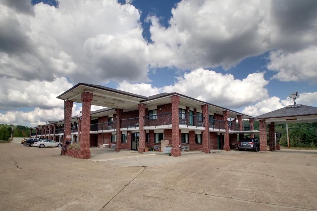 A two-story motel with a brick facade, a covered parking area, and a clear sky.