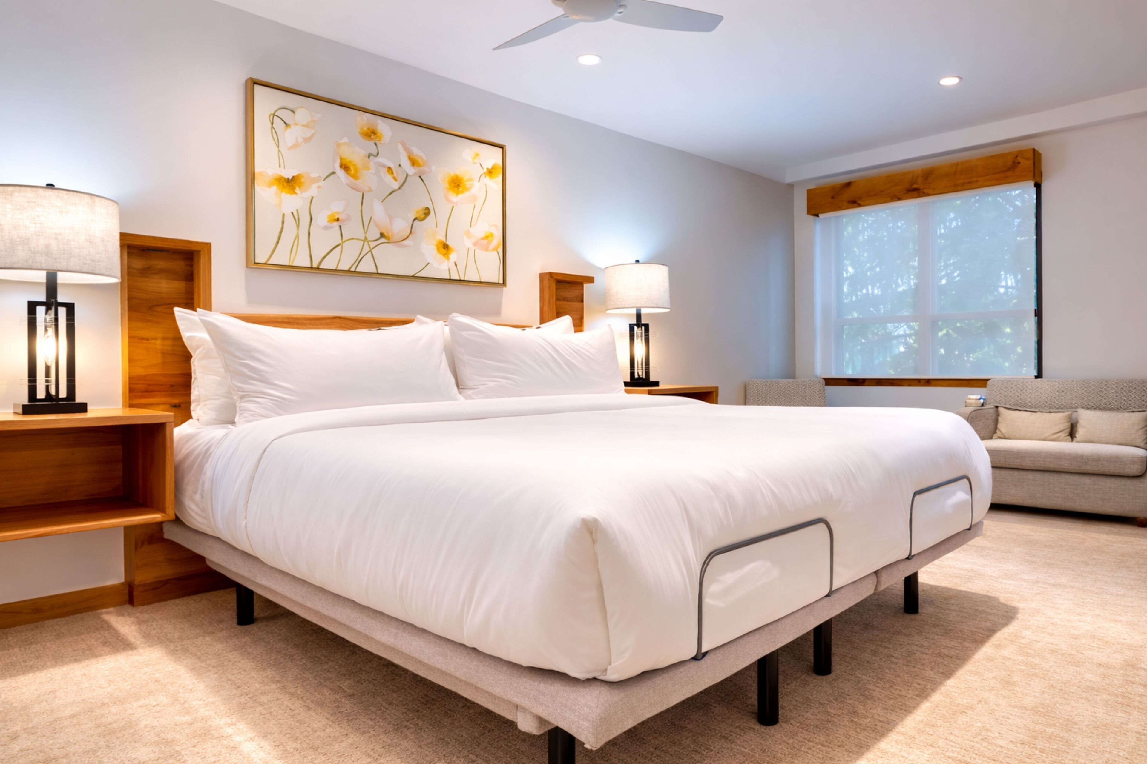 A modern bedroom with a large bed, bedside tables, a nightstand, a wall-mounted lamp, a sofa, and a window with blinds.