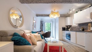 Un salon moderne avec un canapé, une table basse et un tapis rouge. On y trouve une cuisine avec des meubles blancs et un coin repas comprenant une table et des chaises.