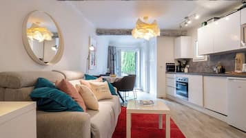 En moderne stue med sofa, sofabord og et rødt tæppe. Der er et køkken med hvide skabe og et spiseområde med et bord og stole.