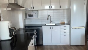 A modern kitchen with white cabinets, a stainless steel range hood, a microwave, a sink, and a refrigerator.