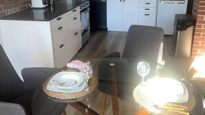 A modern kitchen with white cabinets, a microwave, and a refrigerator. There is a dining table with chairs and a glass top.