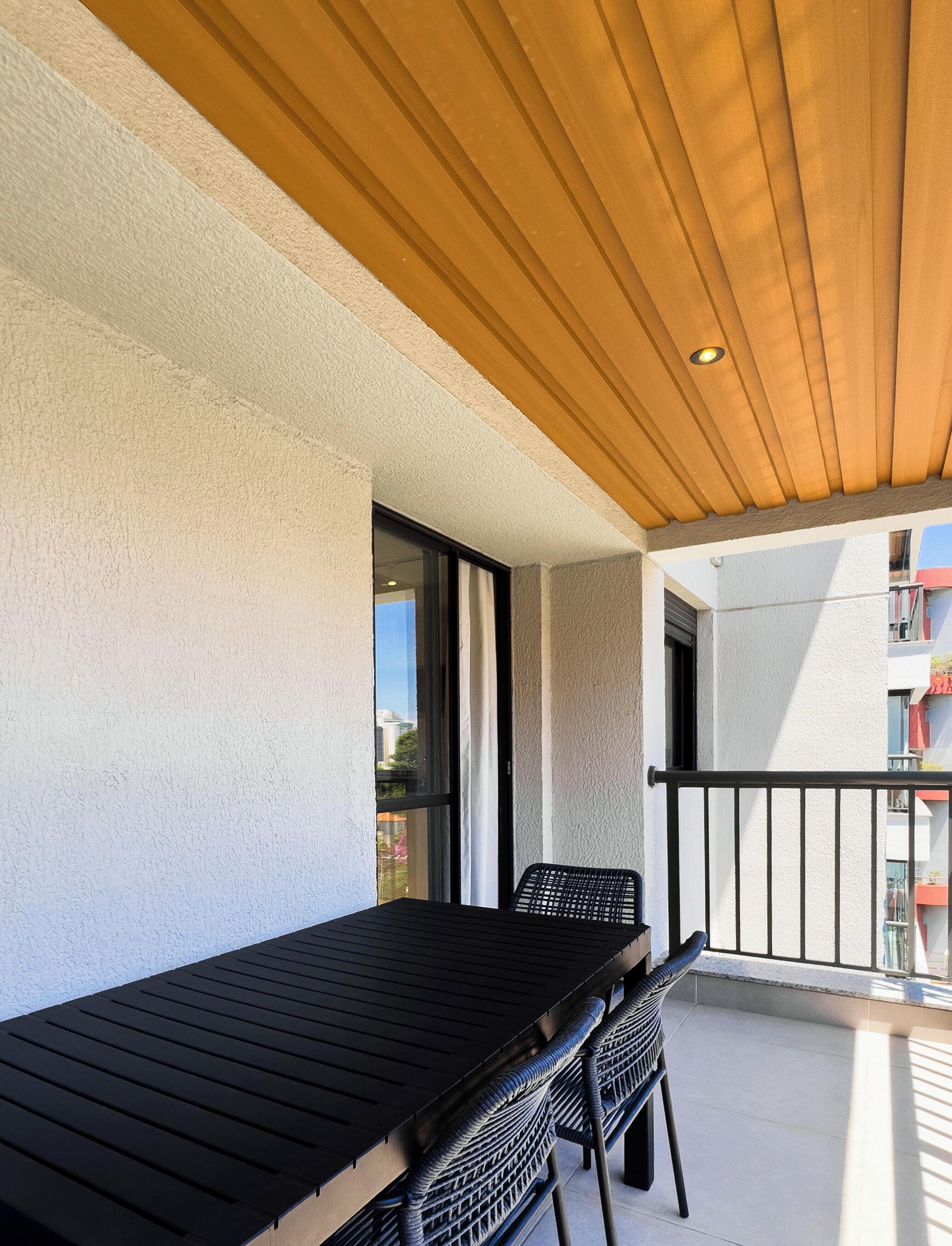 A balcony with a wooden ceiling, a table, and two chairs.