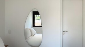 A bedroom with a bed, a white door, and a wall-mounted oval mirror reflecting a window and a sofa. - Update Vila Madalena by Wecare Hosting (São Paulo)