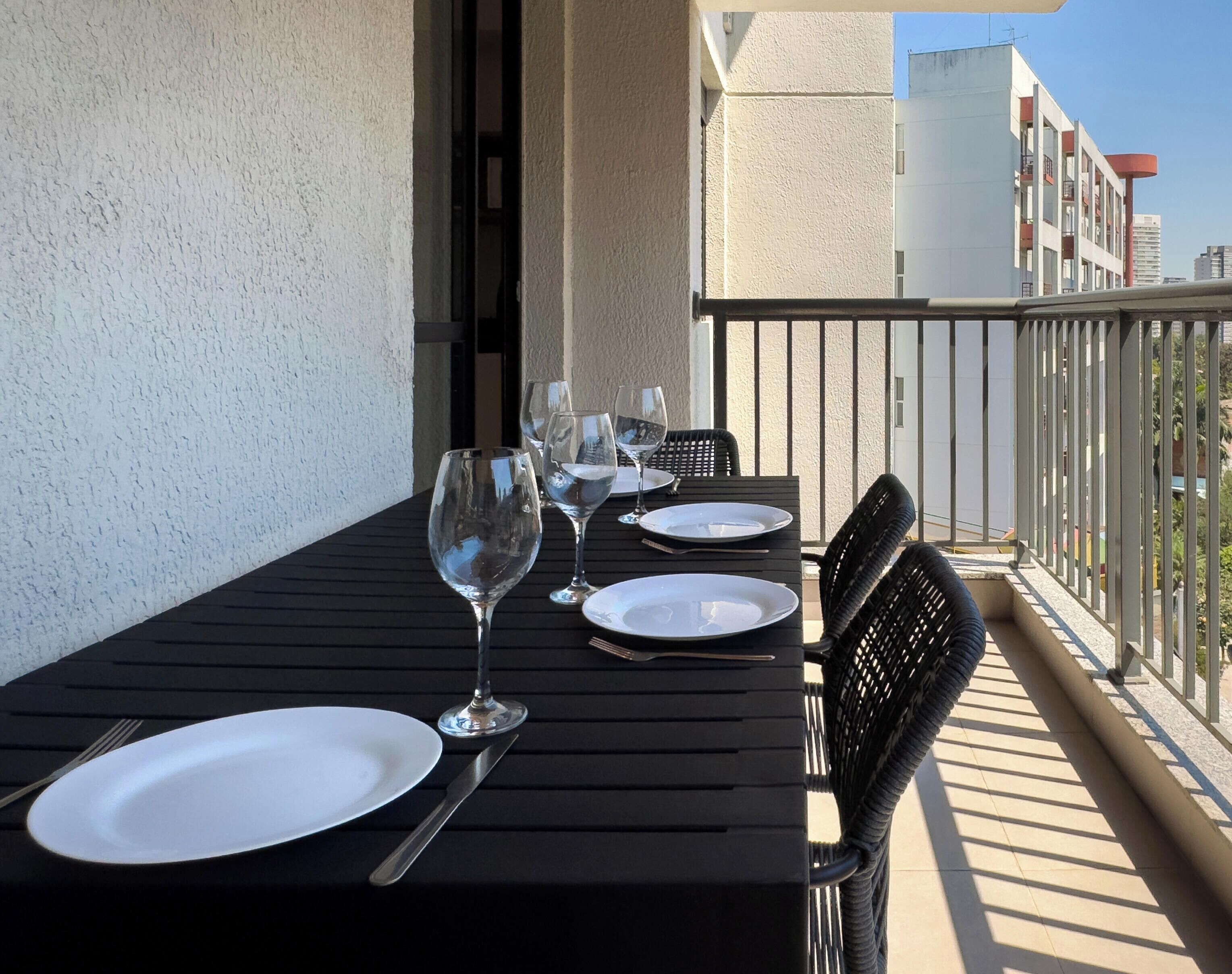 Un balcon avec une table dressée pour le dîner, comprenant des assiettes, des couverts et des verres à vin.
