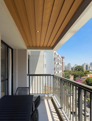 Un balcón con techo de madera, baranda metálica y vista a un paisaje urbano.