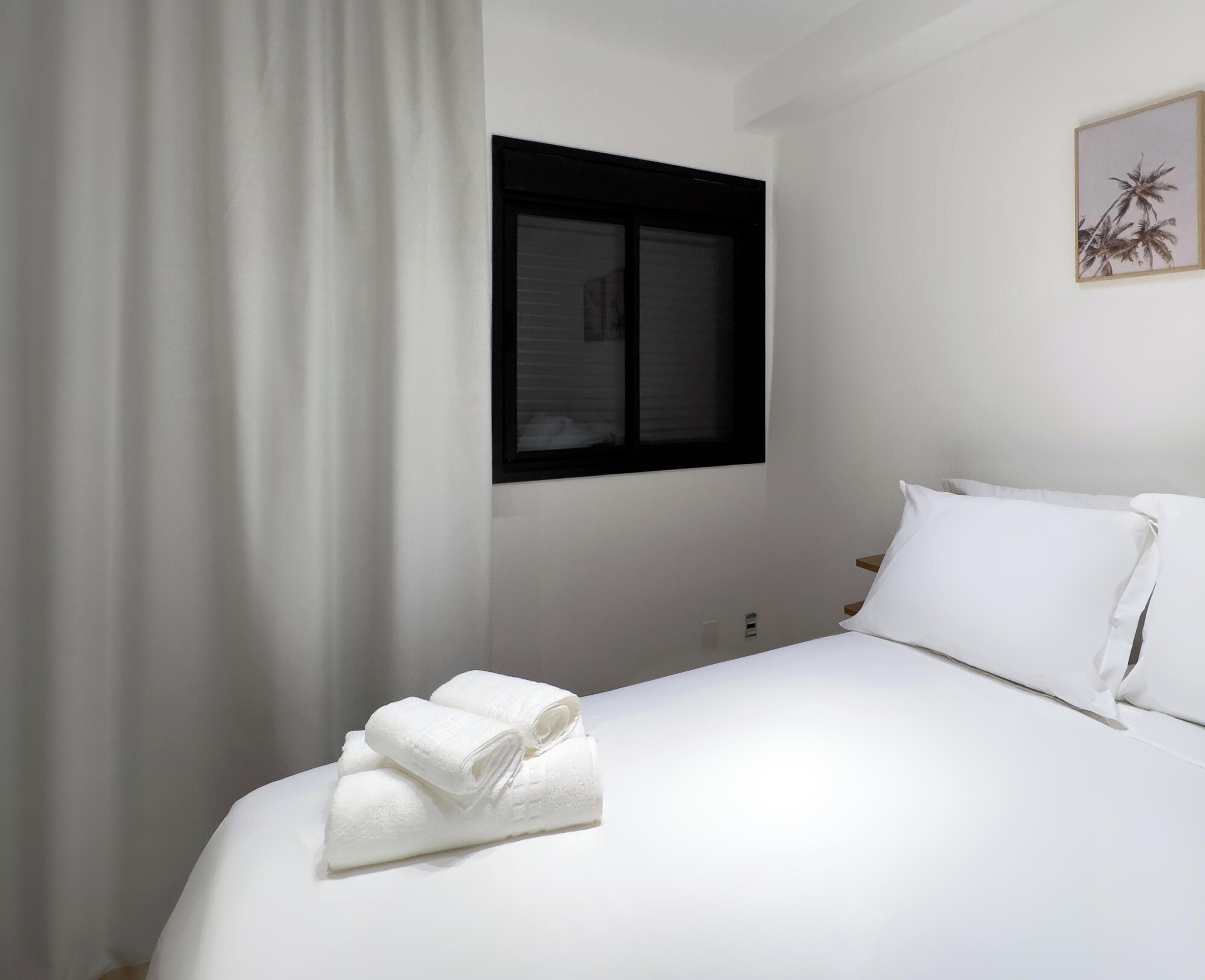 Une chambre d’hôtel avec un lit, des rideaux blancs, une fenêtre et un tableau accroché au mur.