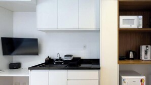 A compact kitchen with white cabinetry, a black countertop, a built-in microwave, and a small refrigerator. - Update Vila Madalena by Wecare Hosting (São Paulo)