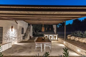 Une terrasse extérieure avec une table et des chaises, une pergola au-dessus et un mur en pierre.