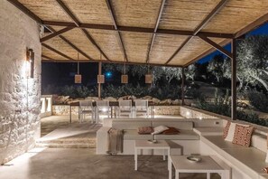Un espace extérieur aménagé avec des sièges, un mur en pierre, un plafond en bois et des lampes suspendues.