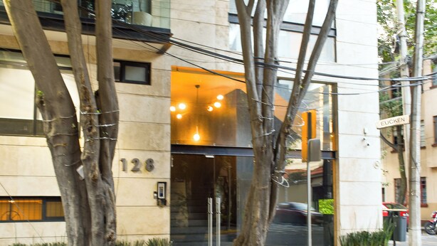 En modern byggnad med en entré av glas, träd framför och en gatukylt med texten ”EUCKEN”.