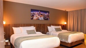 Ett hotellrum med två sängar, sänggavlar i trä, en tavla med en stadsbild på väggen och två vägglampor.