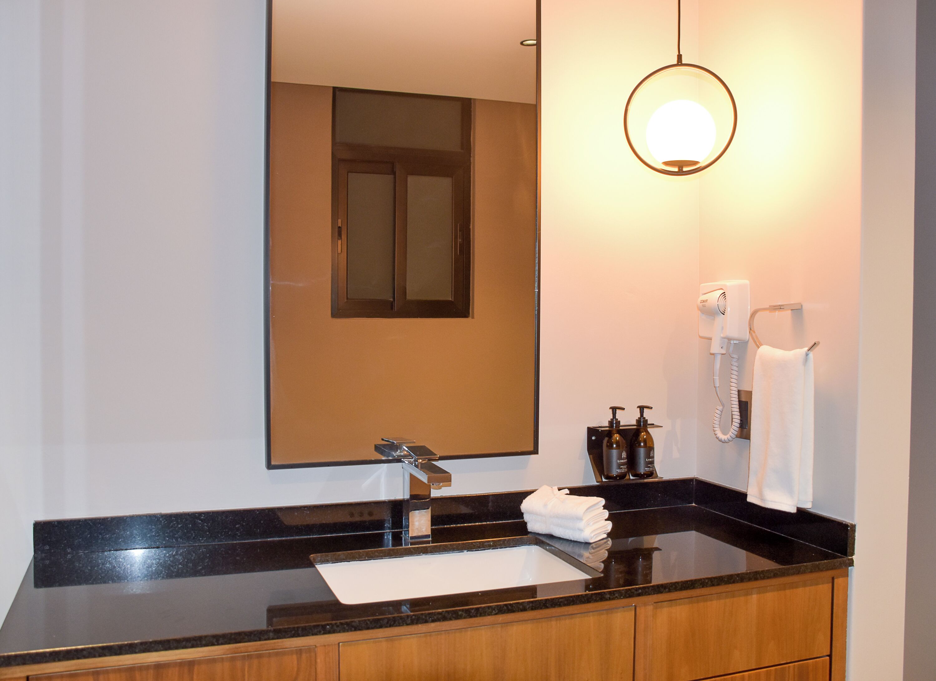 A modern bathroom with a black countertop, a large mirror, a hairdryer, and two bottles of lotion.
