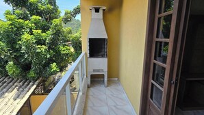 A balcony with a tiled floor, a white grill, and a glass door. - Casa Lagostina 02, Bombinhas Center, 600 meters from the beach. (Bombinhas)