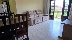 A living room with a sofa, a wooden dining table, and chairs. There is a balcony with a view of buildings. - Casa Lagostina 02, Bombinhas Center, 600 meters from the beach. (Bombinhas)